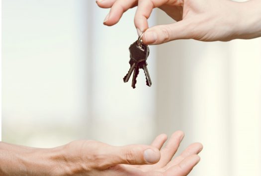 Hand giving set of house keys on blurred background